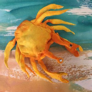 Yellow paperclay crab figurine in a beach painting by Ann James.