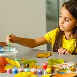 Child dipping paint brush into water and applying paint to leaf cut out